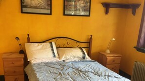 A bed with a blue patterned bedspread, two white pillows, and a folded towel on the footboard. There are two bedside tables with lamps, a wooden nightstand, and a radiator. - Fitzgerald Cape Paterson (Cape Paterson)