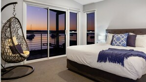 Un dormitorio con cama, una silla colgante y vista al agua.