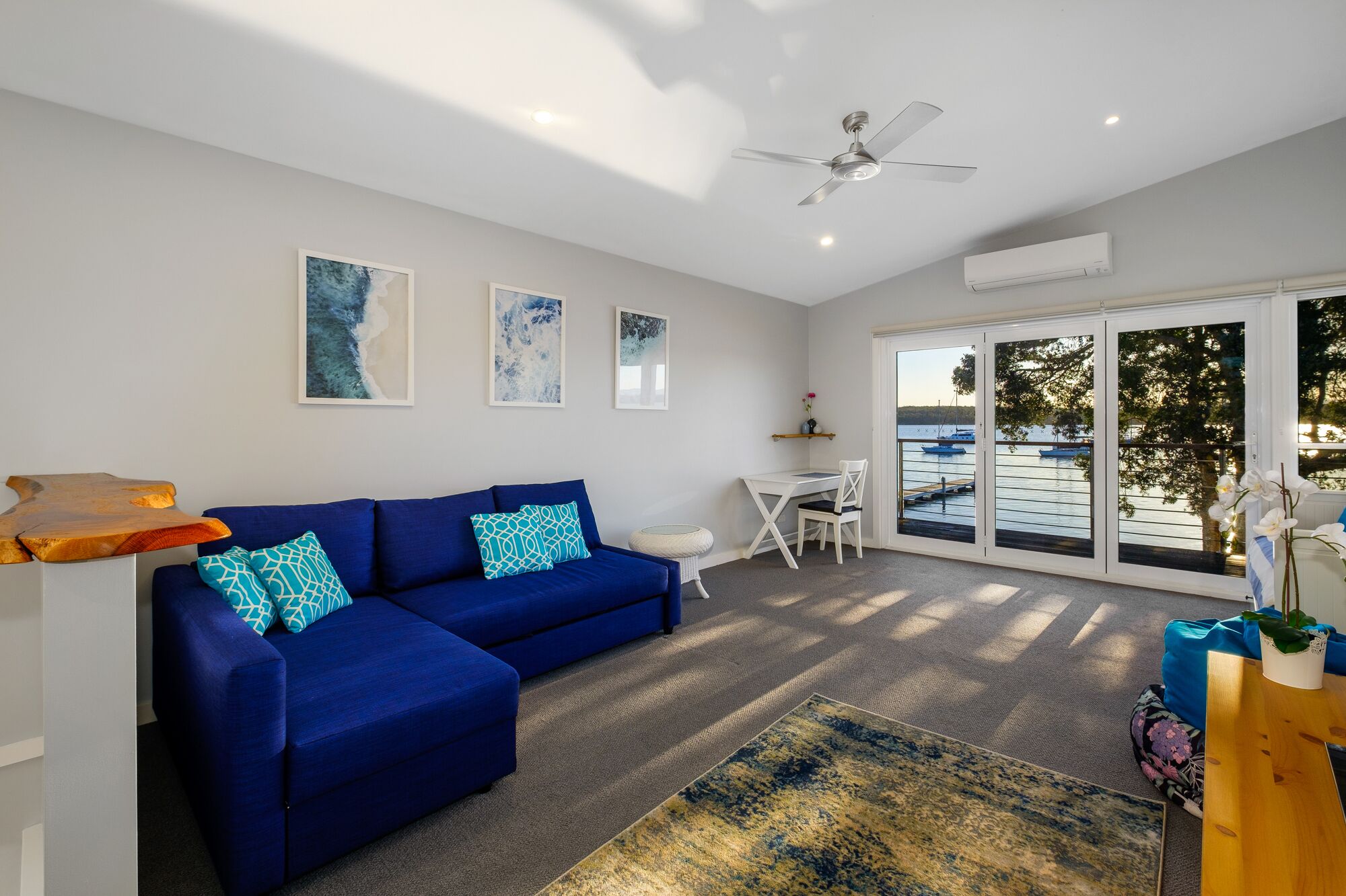 A modern living room with a blue sofa, a coffee table, and a view of the water through large windows.