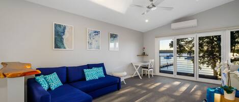 A modern living room with a blue sofa, a coffee table, and a view of the water through large windows.