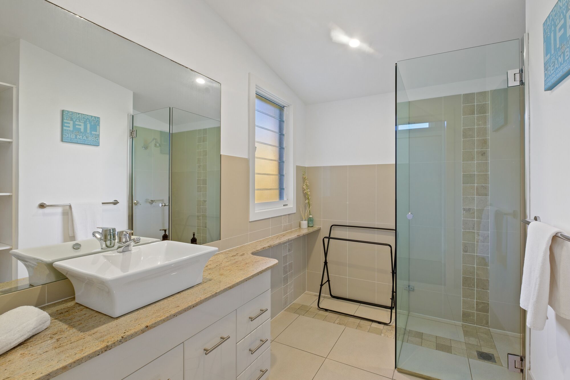 A modern bathroom with a large mirror, a white sink, and a glass shower enclosure.