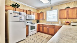Une cuisine avec des meubles en bois, un réfrigérateur, un four à micro-ondes, un four, un évier et une fenêtre avec des stores.