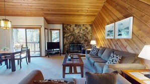 Ein gemütliches Wohnzimmer mit Kamin aus Stein, Holzboden und einem Essbereich mit Fernseher und Tisch.