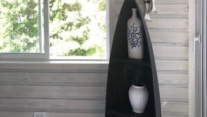 A room with a large window, a surfboard shelf with decorative items, and a view of greenery outside. - Beautiful Beach Front Condo, Club Hemingway, Juan Dolio, D.R (Juan Dolio)
