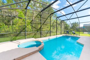 Une piscine intérieure dotée d’une structure en verre, entourée d’une ossature métallique, et une zone herbeuse avec des arbres en arrière-plan.