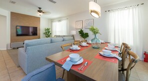 Un salon moderne avec un canapé, une table à manger pour quatre personnes et un téléviseur fixé au mur.