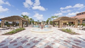 Zona de piscina en un resort con tumbonas, una fuente central y pérgolas.
