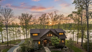A two-story house with a stone pathway leading to the entrance, surrounded by trees and a lake. - Heron Point - Amazing Property with Breathtaking Water Views - Luxury Hot Tub! (Huddleston)