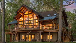 A large, multi-story log cabin with a balcony and a stone foundation. - Heron Point - Amazing Property with Breathtaking Water Views - Luxury Hot Tub! (Huddleston)
