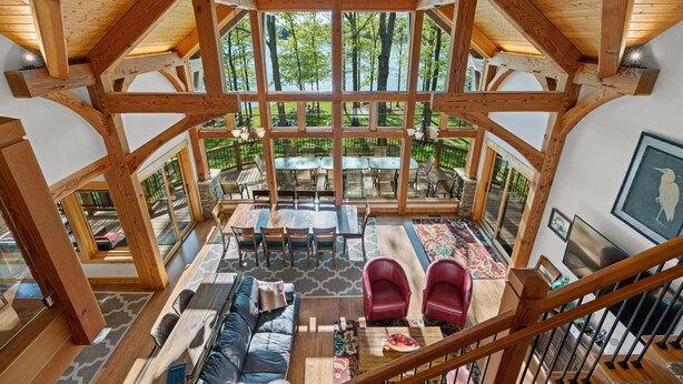 A spacious interior with a high ceiling, wooden beams, a central dining area, and a view of a lake. - Heron Point - Amazing Property with Breathtaking Water Views - Luxury Hot Tub! (Huddleston)