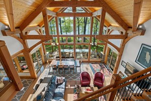 A spacious interior with a high ceiling, wooden beams, a central dining area, and a view of a lake. - Heron Point - Amazing Property with Breathtaking Water Views - Luxury Hot Tub! (Huddleston)