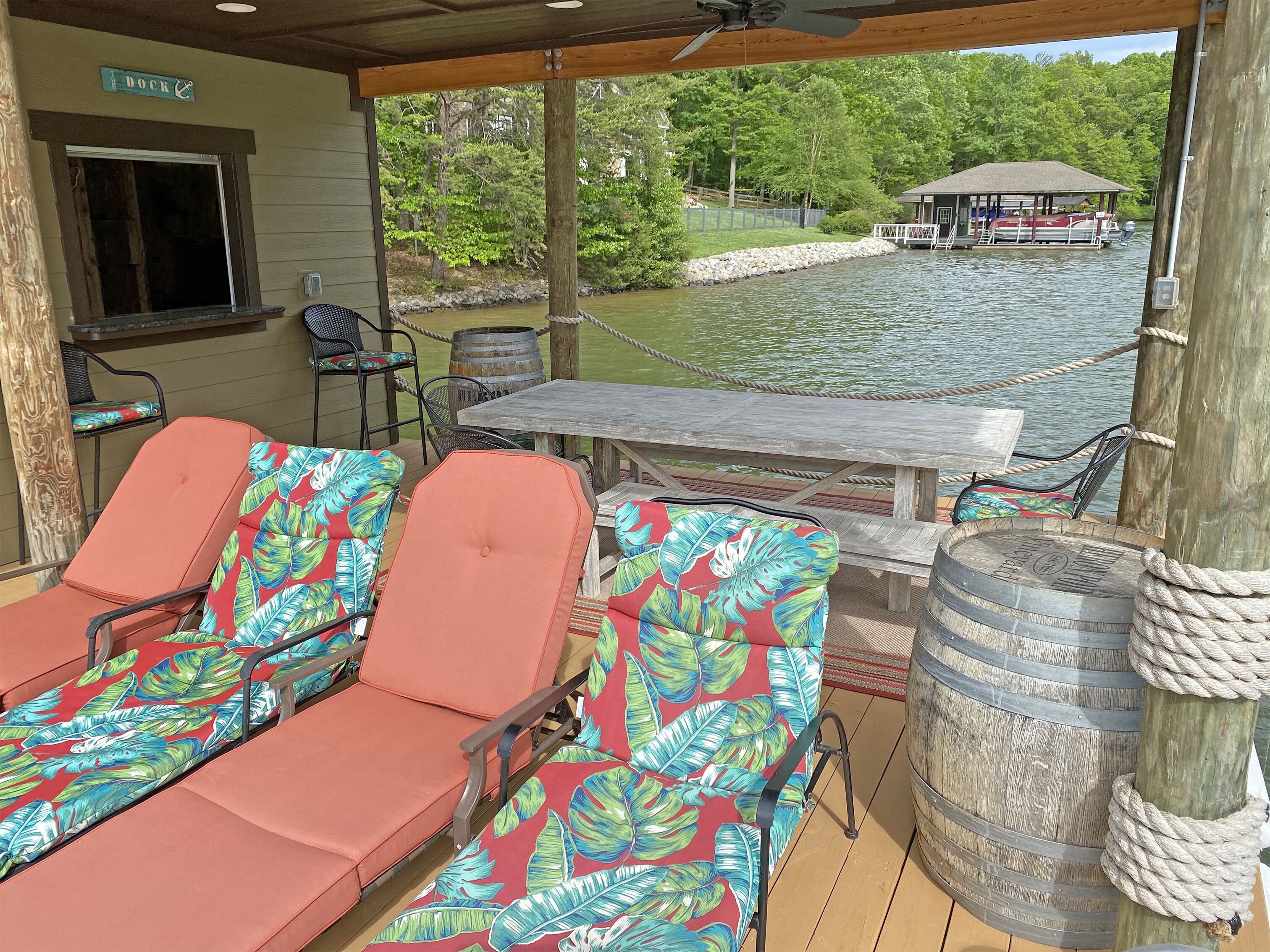 Un espace extérieur aménagé, abrité et doté de fauteuils confortables, d’une table et d’une vue sur un quai et un bateau.