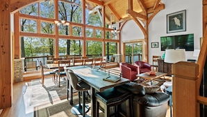A spacious room with large windows, wooden beams, a dining area, and a seating area with a fireplace. - Heron Point - Amazing Property with Breathtaking Water Views - Luxury Hot Tub! (Huddleston)