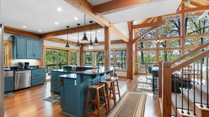 A spacious kitchen with wooden beams, a large island with stools, and a view of the outdoors through large windows. - Heron Point - Amazing Property with Breathtaking Water Views - Luxury Hot Tub! (Huddleston)