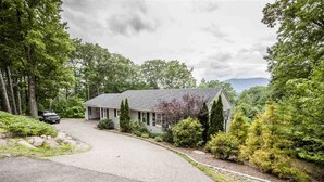 A single-story house with a sloped roof, surrounded by dense greenery and trees. - Family Getaway in N. Conway, Sleeps 16, AC, Hot Tub, Game Room, Pets Welcome (Conway)
