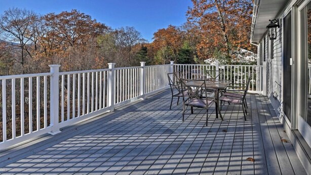 A wooden deck with a white railing, a table with chairs, and a building with a window and a lamp. - Family Getaway in N. Conway, Sleeps 16, AC, Hot Tub, Game Room, Pets Welcome (Conway)