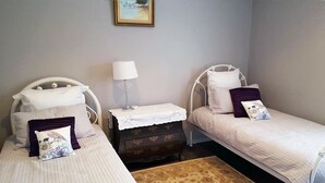 A bedroom with two single beds, a nightstand with a lamp, and a dresser. - Cosy cottage on mair (Ballarat)