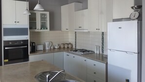 A modern kitchen with white cabinets, a stainless steel sink, a gas stove, and a refrigerator. - Cosy cottage on mair (Ballarat)