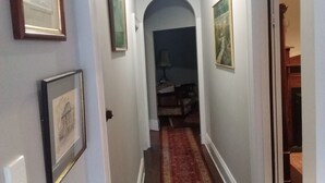 A narrow hallway with framed artwork on the walls, a red carpet, and an arched doorway leading to another room. - Cosy cottage on mair (Ballarat)