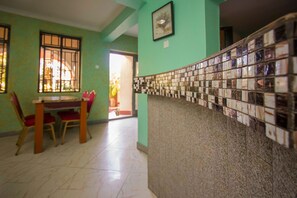 A room with a tiled wall, a wooden table with chairs, and a window with bars.