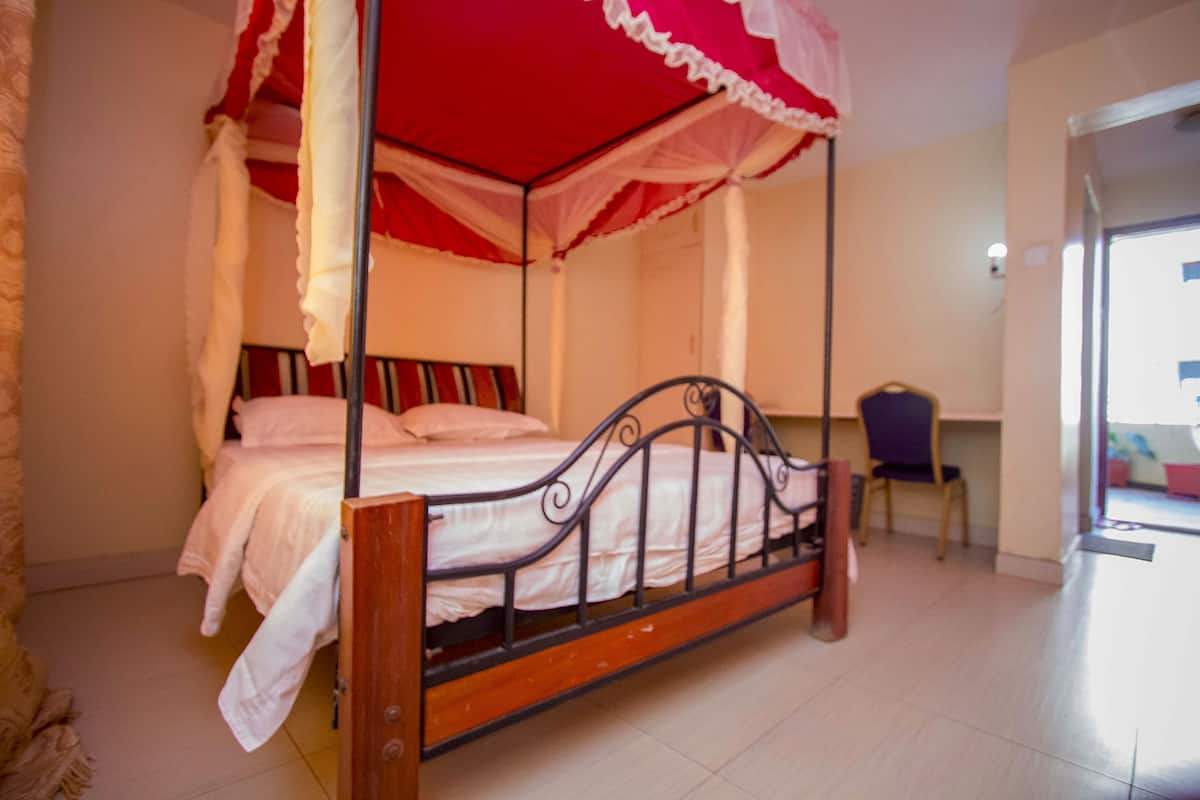 Una cama con dosel, una silla y una mesita de noche en una habitación con paredes blancas y suelo de baldosas.
