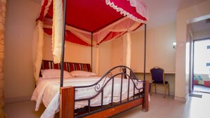 Una cama con dosel, una silla y una mesita de noche en una habitación con suelo de baldosas y una puerta que da a otra estancia.