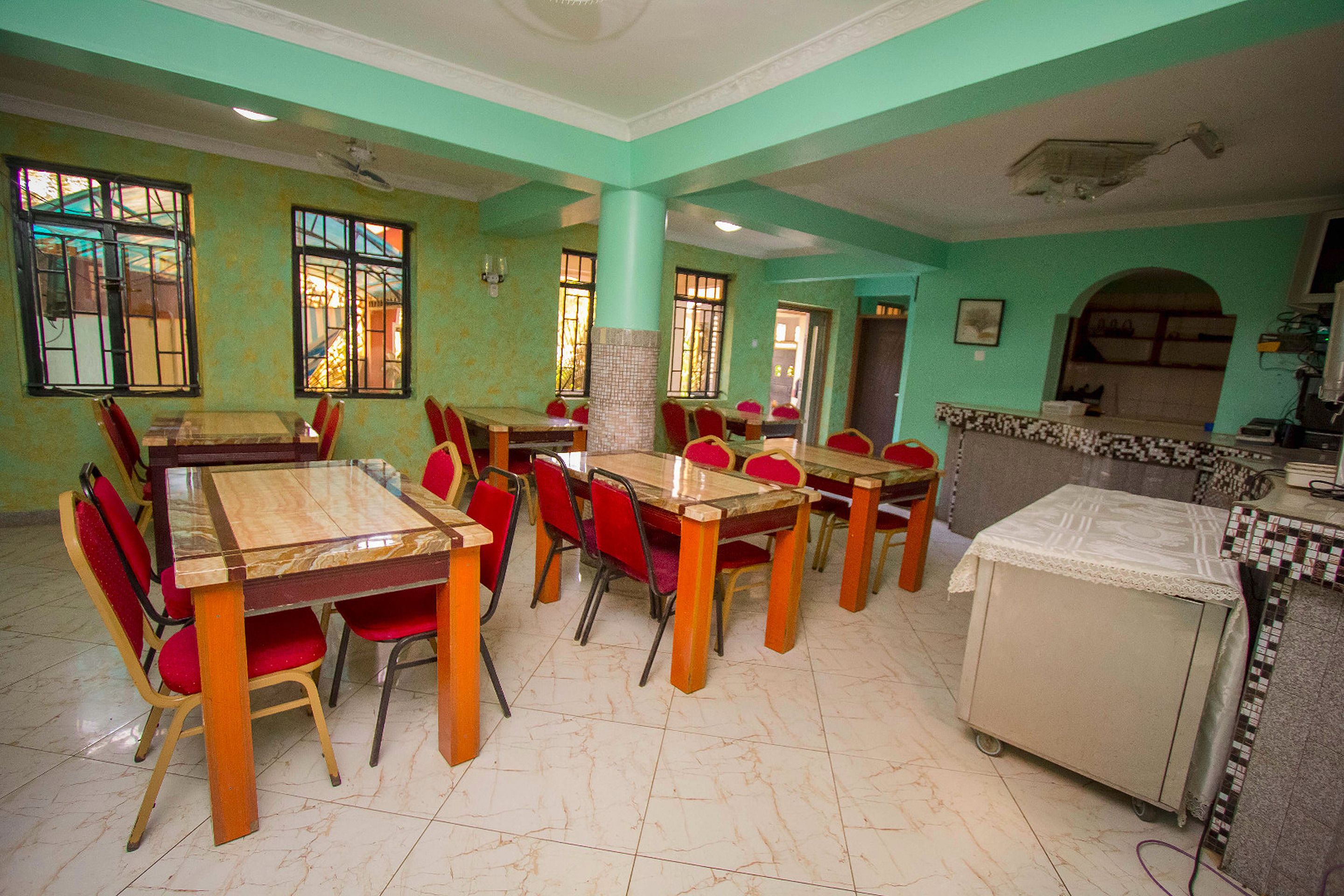 A dining area with multiple tables and chairs, a kitchen area with a counter, and a tiled floor.