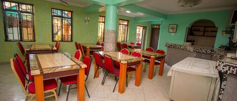A dining area with multiple tables and chairs, a kitchen area with a counter, and a tiled floor.