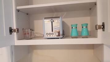 A kitchen cabinet with a toaster, a measuring cup, and two teal-colored containers.