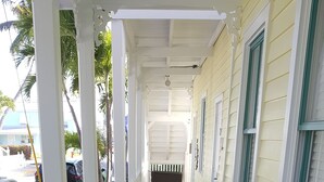 Um deck de madeira coberto com grades brancas, que leva a um edifício com janelas emolduradas a verde.