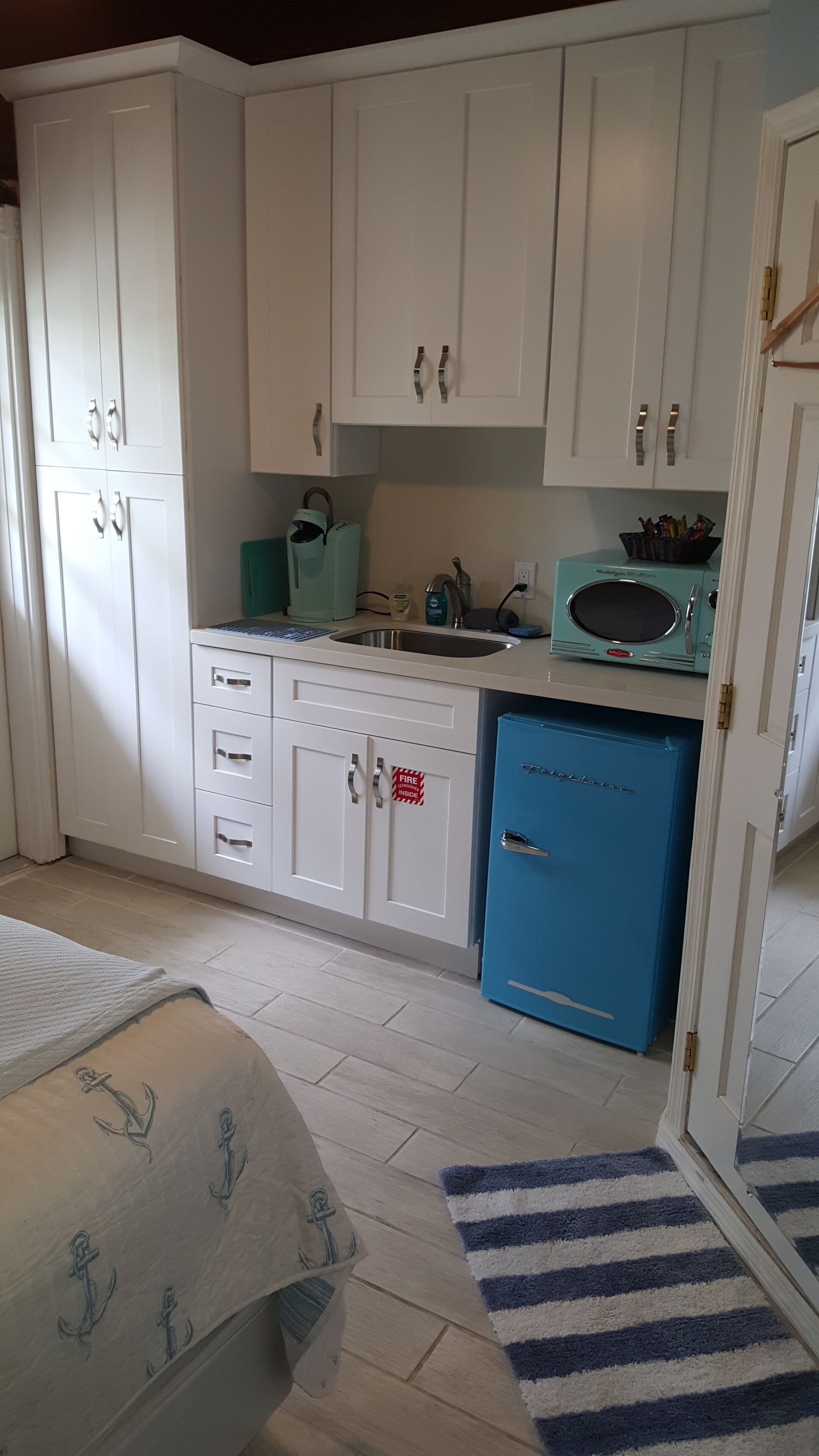 Eine Küche mit weißen Schränken, einem blauen Kühlschrank, einer Spüle und einer Mikrowelle.