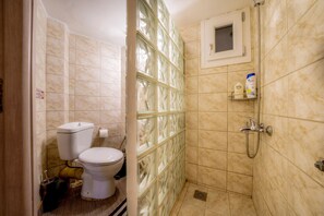 A bathroom with a toilet, a shower with a glass partition, and a small cabinet with toiletries. - Kentrikon Deluxe Apt Must (Thessaloniki)