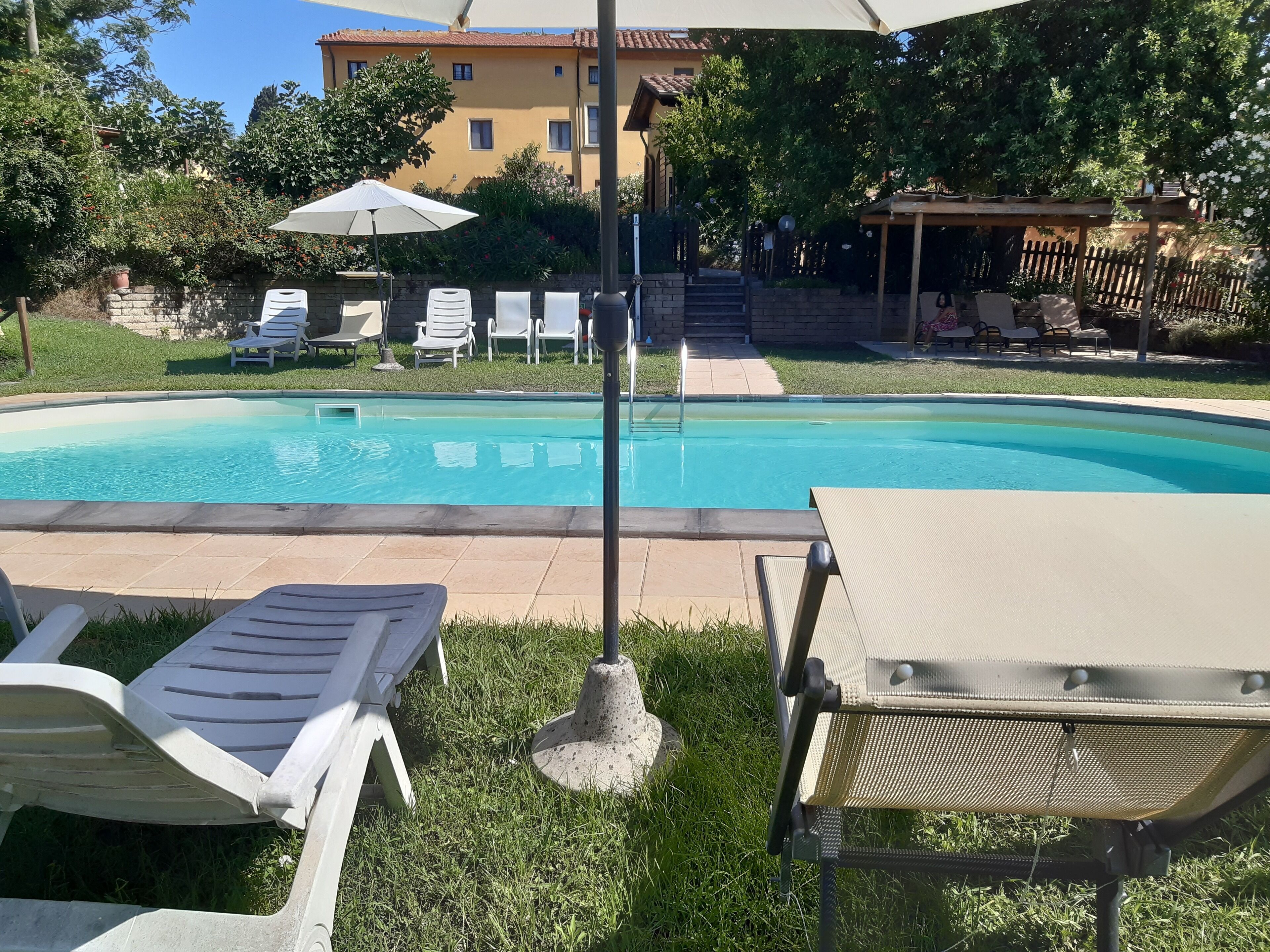 A swimming pool with lounge chairs and umbrellas, surrounded by a garden and a building.