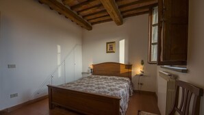 A bedroom with a wooden bed, a chair, a radiator, a window, and a staircase.