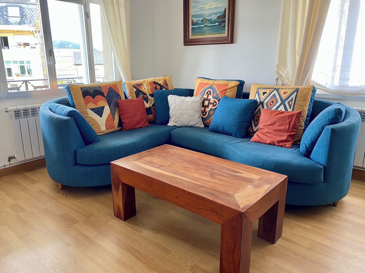 A blue sofa with patterned cushions, a wooden coffee table, and a painting on the wall.