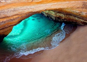 Een natuurlijke rotsformatie met een zwembad helder water en een zandstrand.
