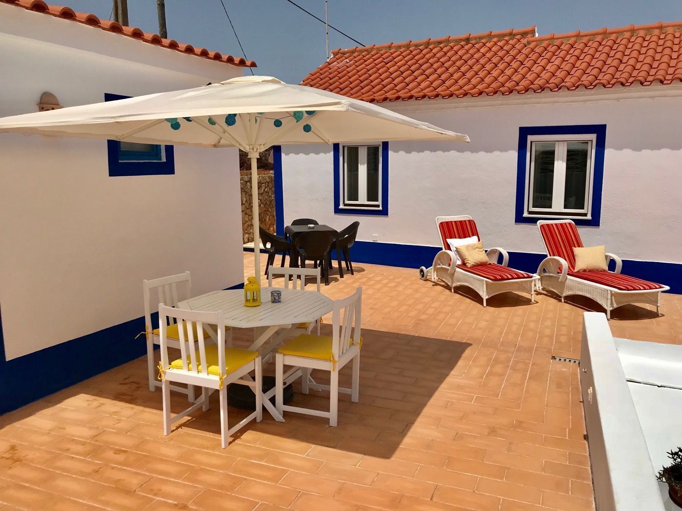 A patio with a table and chairs, a sun umbrella, and two lounge chairs.
