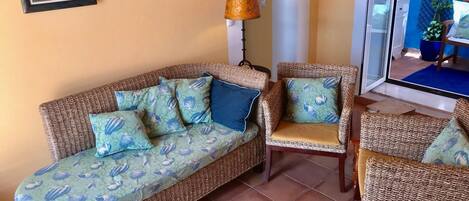 A living room with a wicker sofa, matching armchairs, and a patterned cushion.