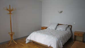 A bedroom with a bed, a wooden floor, a nightstand, a bedside table, and a coat rack. - Between sea and countryside (Saint-Gatien-Des-Bois)