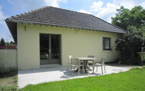 Un bâtiment d’un seul étage, doté d’un toit en tuiles, d’une porte-fenêtre coulissante et d’un petit espace patio avec une table et des chaises.