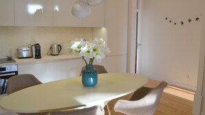 Een moderne keuken met witte kasten, een eettafel met stoelen, een blauwe vaas met witte bloemen en een plafondlamp.