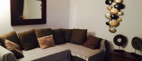 A living room with a sectional sofa, a mirror, and a wall-mounted decorative piece.
