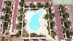 Vue aérienne d’un hôtel doté d’une piscine centrale, entourée de palmiers et d’espaces de détente.