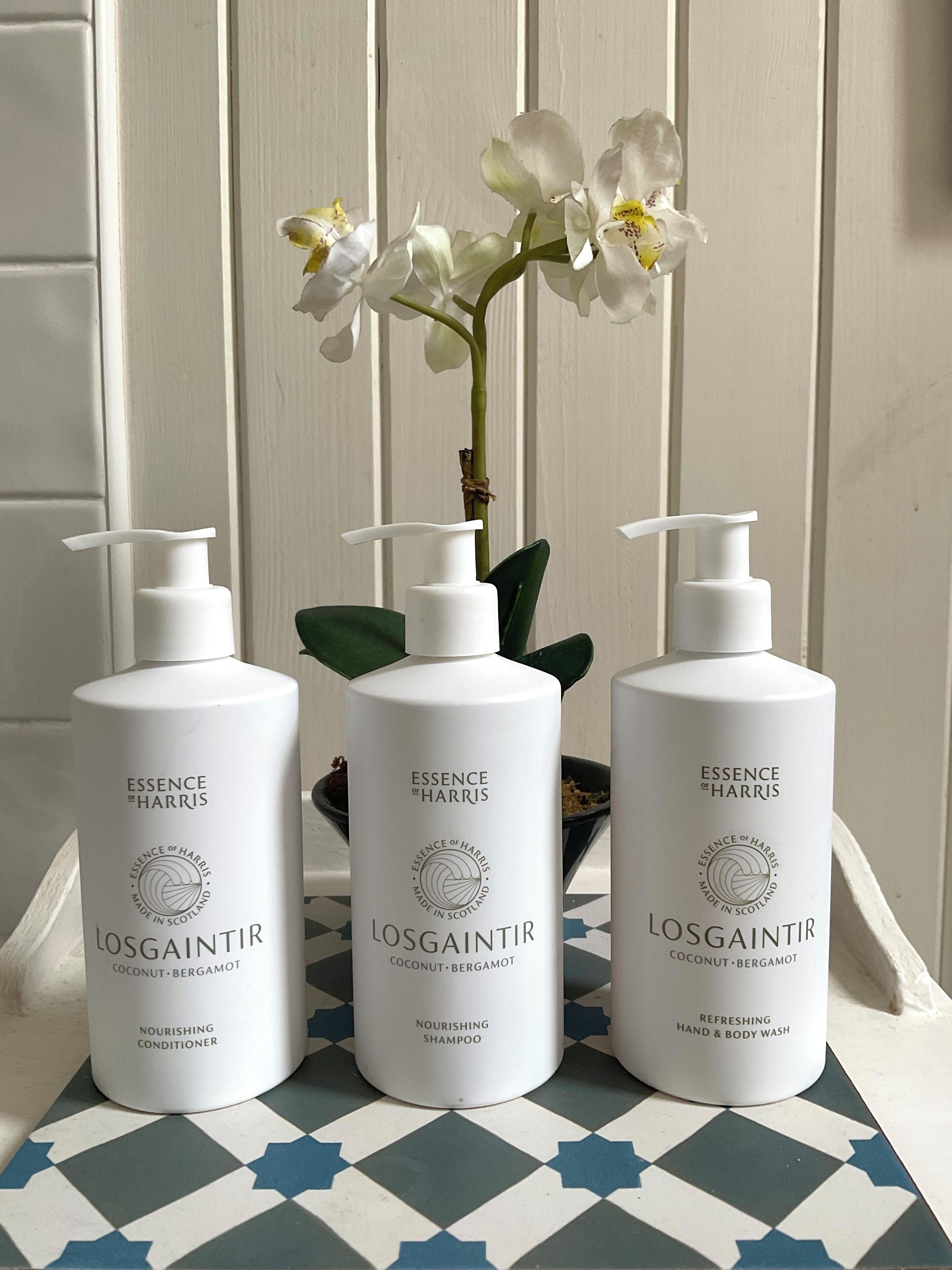 Three bottles of Essence of Harris products on a tiled surface with a white orchid in the background.