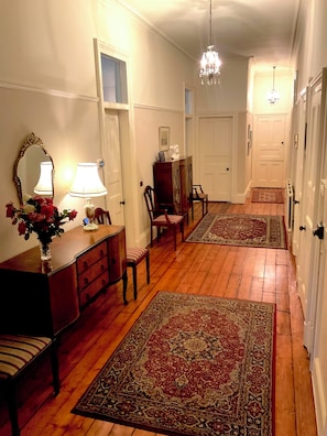 A hallway with wooden flooring, a chandelier, a desk with a vase of flowers, and two chairs.