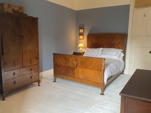 A bedroom with a wooden bed, a nightstand with a lamp, a wardrobe, and a door.