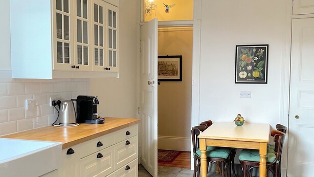 Une cuisine avec des meubles blancs, un plan de travail en bois et un coin repas comprenant une table et des chaises.