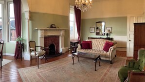 Un salon traditionnel avec une cheminée, un canapé, un fauteuil vert et un lustre.