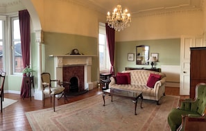 A traditional living room with a fireplace, a sofa, a green armchair, and a chandelier.