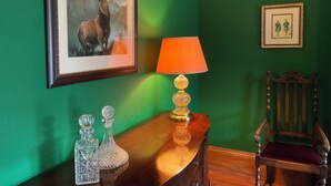 Une pièce avec un mur vert, un tableau représentant un cerf encadré, une table avec une lampe et une chaise en bois.
